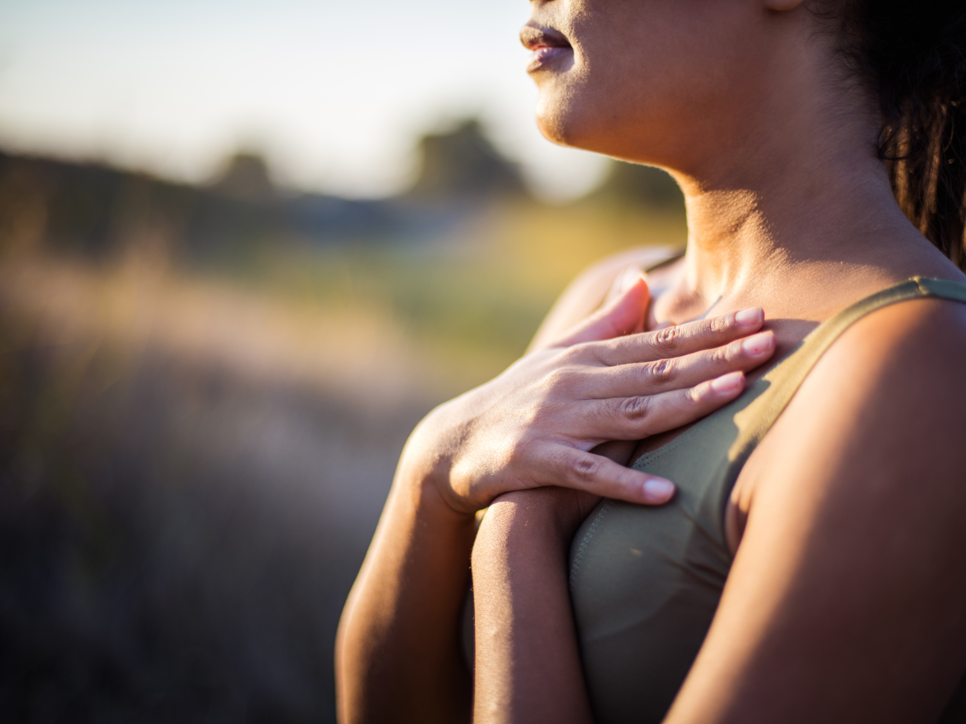 Woman with hands on heart, expressing gratitude and mindfulness in nature.